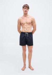 Σκούρα μπλε ναυτικά μαγιό σορτς με ελαστική ζώνη μέσης και λευκό κορδόνι. Ελαφρύ ύφασμα, μήκος πάνω από το γόνατο, ελάχιστη σήμανση.