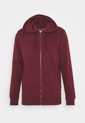 Bordeauxroter Kapuzenpullover mit durchgehendem Reißverschluss, Fronttaschen, Kordelzug an der Kapuze, gerippten Bündchen und Saum sowie dezentem Logo auf der Brust vor einfarbigem Hintergrund.