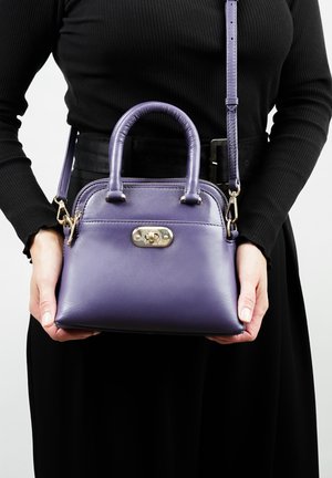 Paarse leren handtas met dubbele handvatten en een afneembare schouderband, met gouden details en een ritssluiting. Glad textuur en gestructureerde vorm.