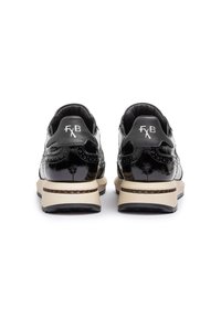 Zapatillas de charol negro con detalles de brogue, logo blanco en el talón y suela de goma beige con un acabado texturizado.