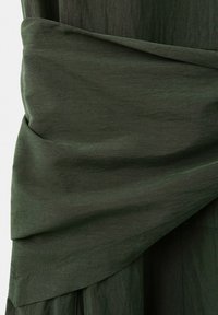 Material verde închis cu pliuri stratificate și detaliu texturat de cusătură pe un material moale, ușor cutat.