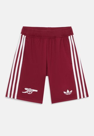 Burgundijas sporta šorti ar platu baltu elastīgu jostiņu, kuros katrā pusē ir trīs baltas svītras un iešūti balti logotipi.