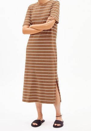 Robe rayée marron à manches courtes, avec des rayures blanches horizontales, une silhouette droite et des fentes latérales. Portée avec des sandales noires à enfiler.