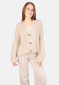 Beige gestrickte Strickjacke mit V-Ausschnitt, drei dekorativen Knöpfen und voluminösen Ärmeln; aus einem weichen, strukturierten Garn hergestellt.