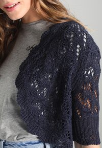 Granatowe dzianinowe bolerko z koronkowym wzorem i krótkimi rękawami, noszone na szarej koszuli. Charakteryzuje się fakturowaną przędzą i otwartym splotem.