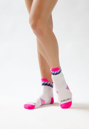 Legs crossed wearing white ankle socks with bright pink heels, toes, and striped blue and purple cuffs on a white background.