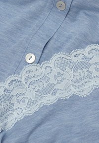 Hellblauer Stoff mit weißer Blumen-Spitzenbesatz und zwei weißen Knöpfen, die entlang einer Naht angenäht sind.