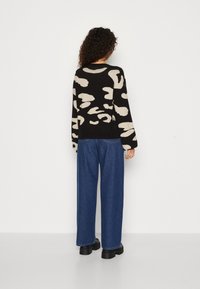 Schwarzer Pullover mit beigem abstraktem Muster, lockere Passform, lange Ärmel, kombiniert mit weiten blauen Jeans und schwarzen klobigen Schuhen.