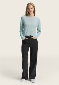Pull albastru deschis, cu mâneci lungi și croială lejeră, purtat cu blugi negri, cu talie înaltă și pantaloni largi, și teniși albi. Fundal neutru.