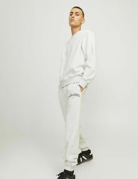 Felpa grigia e pantaloni jogger abbinati realizzati in tessuto morbido, con polsini a costine e il logo "Jack & Jones" sui pantaloni. Scarpe da ginnastica nere.