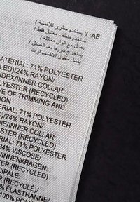 Étiquette de soin du vêtement indiquant la composition du tissu en anglais et en arabe, listant le polyester, le rayonne, la viscose et les matériaux recyclés.