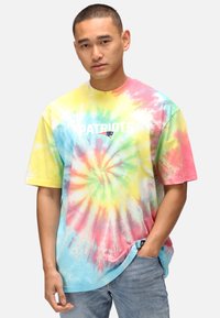 Tie-dye t-shirt med en virvel av pastellfärger: gul, rosa, grön och blå. "PATRIOTS" logotyp i vitt i mitten. Korta ärmar.
