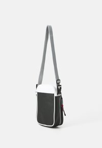Borsa a tracolla bianca e nera con tracolla grigia, materiale liscio, chiusura a zip e dettaglio rosa. Forma rettangolare con angoli arrotondati.