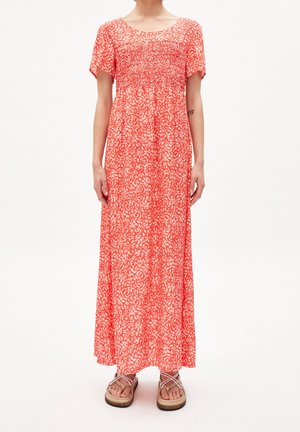 Femme portant une robe longue corail à fleurs jusqu'aux chevilles, à manches courtes, poitrine smockée, et des sandales compensées beiges.