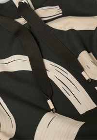 Schwarzer Stoff mit beigefarbenem abstraktem Pinselstrichmuster. Verfügt über schwarze Kordeln mit cremefarbenen Enden und eine weiche Textur.