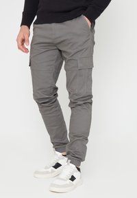 Grijze cargo broek met elastische boorden, meerdere zijzakken en een gladde, licht gestructureerde stof. In combinatie met witte sneakers met zwarte accenten.