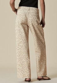 Beige vida jeans med en subtil leopardprint, med bakfickor och ett något strukturerat tyg för extra detalj.