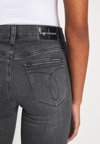 Jeans de mezclilla gris con un diseño ajustado, que cuentan con un parche de logo en la cinturilla y costuras distintivas en los bolsillos traseros.
