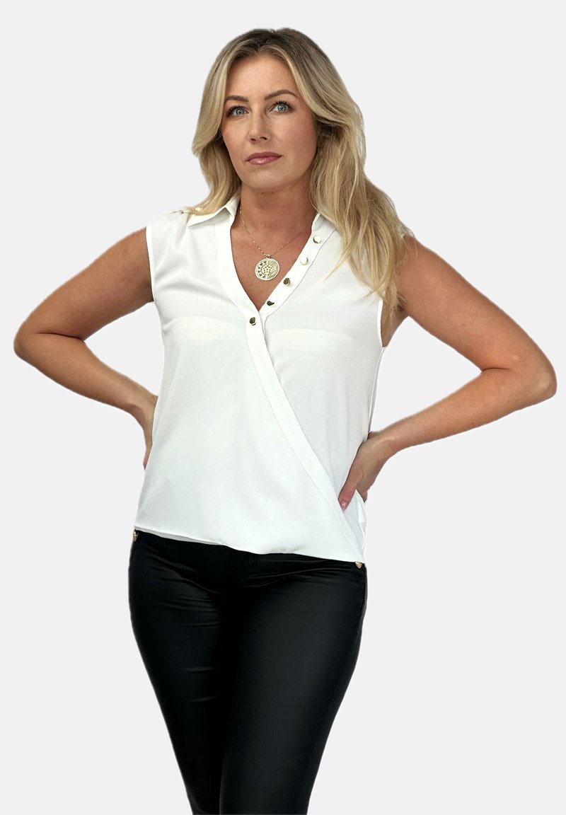 Biała bluzka bez rękawów z kołnierzykiem, ozdobiona guzikami po jednej stronie i mająca ukośny krój, w zestawie z czarnymi spodniami.