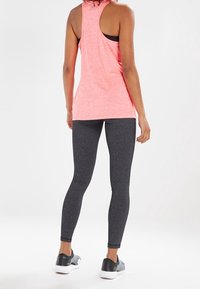 Leggings grigi aderenti abbinati a una maglietta rosa senza maniche, con design a bralette, realizzata in tessuto elasticizzato e traspirante.