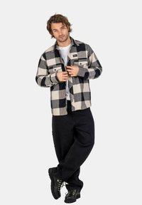 Black and white checkered flannel shirt with two front pockets, button-down closure, and a relaxed fit, paired with black jeans and boots.