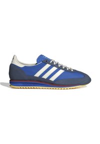 Blue athletic shoes with a textured grey toe cap, three white stripes, and a rubber outsole featuring multi-directional lugs.