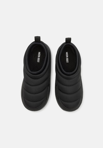 Chaussures noires à enfiler avec un design matelassé, fabriquées à partir d'un matériau doux et rembourré, avec une semelle texturée et des tirettes pour un enfilage facile.
