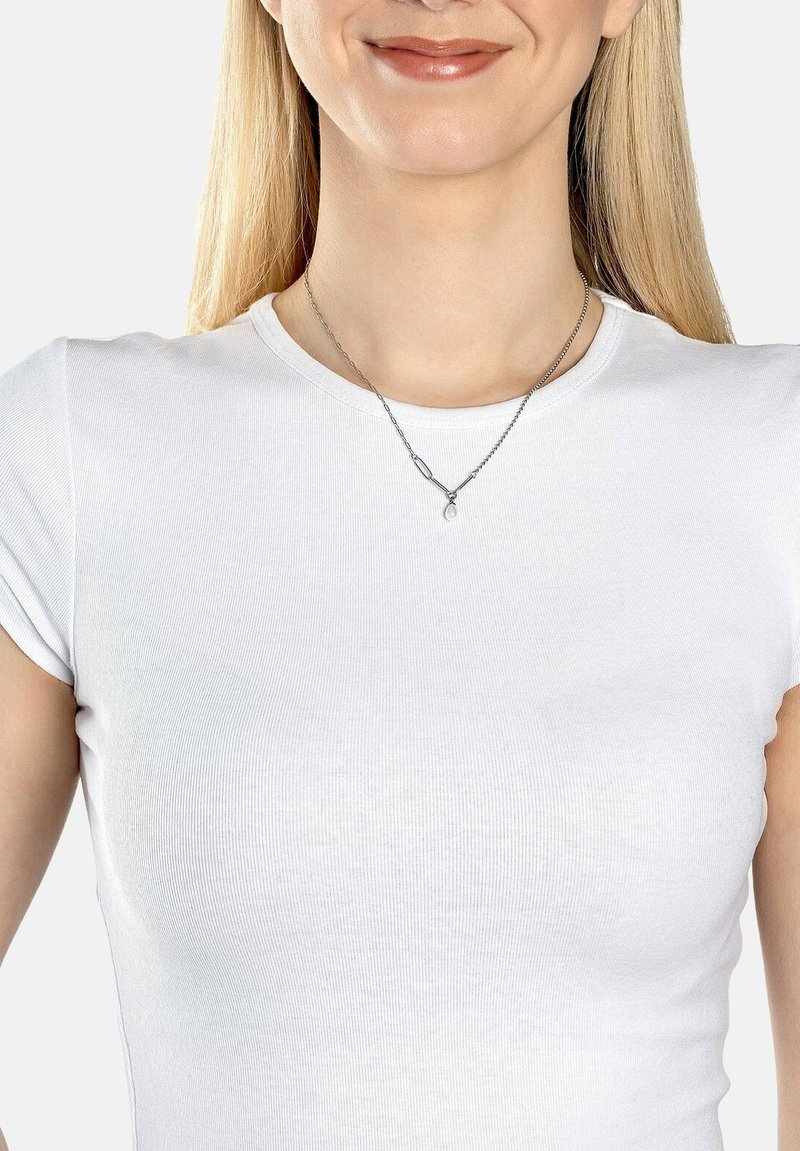 Sølv halskæde med en dråbeformet vedhæng, båret over en tætsiddende hvid ribbet t-shirt, der fremhæver kædens tekstur og delikate design.
