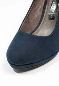 Chaussure à talon haut en daim bleu marine avec un bout rond et une finition lisse et élégante. L'intérieur présente un matériau doux et contrastant.