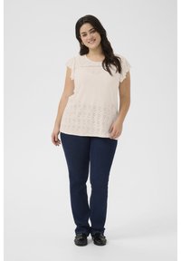 Haut rose pâle à manches courtes avec un motif à œillets et des manches volantées, associé à un jean droit bleu foncé et des chaussures noires à enfiler.