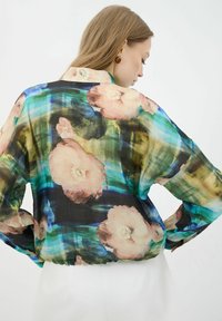 Blusa floral transparente con un corte holgado, que presenta un patrón multicolor de grandes flores rosas y acentos en azul verdoso. Detalle de dobladillo elástico.