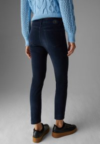 Mörka jeans med skräddarsydd passform, bakfickor och en svart logotyp-patch på midjebandet. Matchas med svarta plattformsskor.