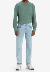 Zelená košile s dlouhým rukávem a kulatým výstřihem, doplněná o světle modré džíny a bílé tenisky s červenými akcenty. Ležérní, uvolněný střih.