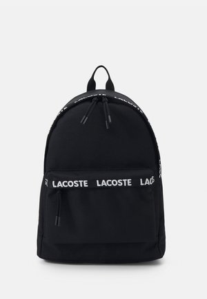 Sort rygsæk med en glat overflade, der har en frontlomme med lynlås og et logo-bånd. Justerbare stropper og et håndtag på toppen til bæring.