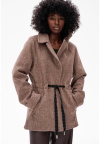 Bruine, gestructureerde wollen jas met een omslagkragen, een ceintuur in de taille en zijzakken. Heeft een ontspannen pasvorm en zwarte trekkoordaccenten.