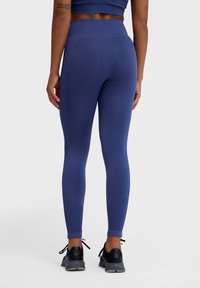 Navyblaue Leggings aus dehnbarem Material mit hohem Bund und Knöchel-Details mit verstellbaren Bändern. Glatte Textur, taillierte Passform.