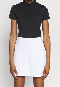 Czarna koszulka polo z krótkimi rękawami, pięciozapinana na guziki, oraz biała spódnica o gładkiej fakturze z subtelnym logo Nike na talii.