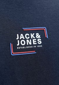 Camiseta azul marino con textura suave; presenta el texto "JACK & JONES" en blanco y colores, en negrita, con acentos de líneas rojas y azules.