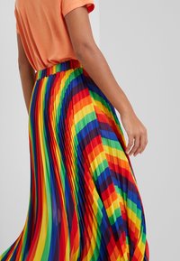 Jupe maxi plissée présentant des rayures verticales aux couleurs vives de l'arc-en-ciel, fabriquée dans un matériau léger au toucher lisse.