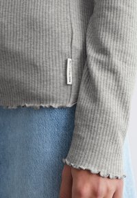 Grijze geribbelde trui met een cropped ontwerp, met golvende manchetten en een klein label met de tekst "Marc O'Polo Denim." Draag over een lichte denim rok.
