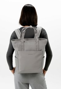 Grå ryggsäck med dubbla handtag på toppen och justerbara remmar. Har två sidofickor och en minimalistisk design. Tillverkad av hållbart material.