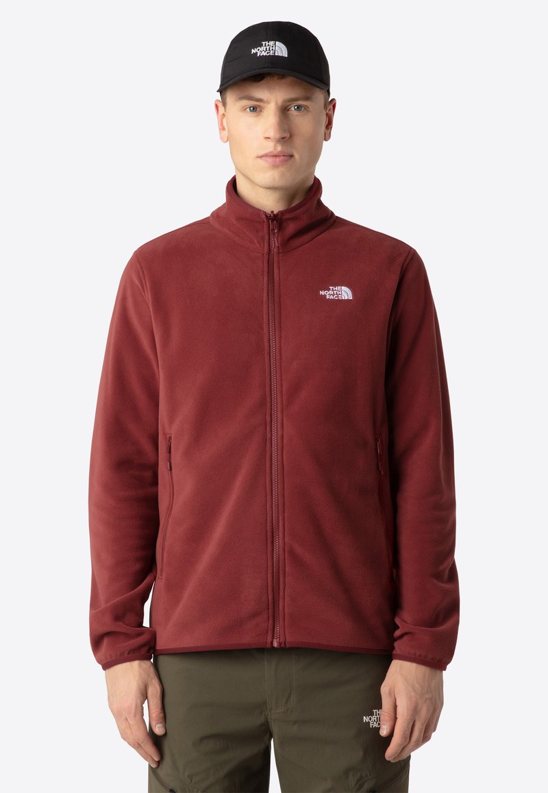 Giacca in pile color bordeaux con colletto alto, chiusura con zip e tasche laterali. Presenta un piccolo logo bianco sul lato sinistro del petto.
