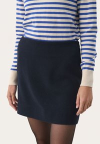 Jupe mini marine avec une texture lisse, associée à un haut à manches longues rayé bleu et blanc et des collants noirs transparents.