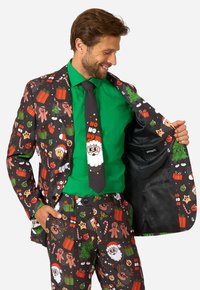 Krāsains uzvalks ar Ziemassvētku motīviem melnā krāsā, kurā attēloti Santa, piparkūku vīri un dāvanas. Apvienots ar zaļu krekli un atbilstošu kaklasaiti.