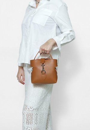 Brown leather bucket bag with a structured shape, featuring a top handle, metallic hardware, and a heart-shaped accent hanging from the clasp.