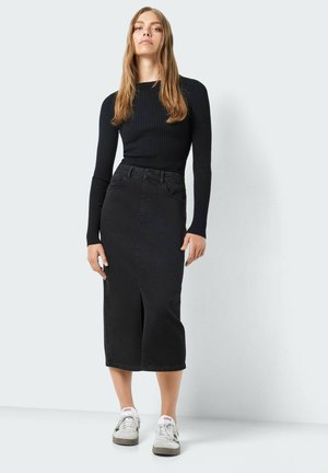 Haut noir à rayures côtelées à manches longues associé à une jupe en denim noire avec une fente à l'avant. Le modèle porte des baskets blanches et grises.
