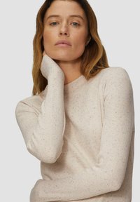 Hellbeige langärmliger Pullover mit gerippter Textur, ausgestattet mit bunten Sprenkeln. Rundhalsausschnitt und eng anliegende Ärmel.
