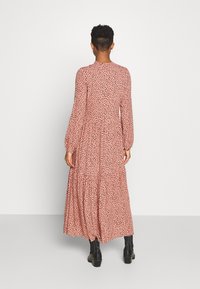 Dlouhé růžové šaty s černým puntíkovaným vzorem, s dlouhými rukávy, vysokým výstřihem a vrstvenou, splývavou sukní. Nosit je s černou obuví.