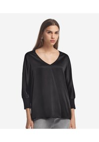 Schwarze Satinbluse mit langen Ärmeln, V-Ausschnitt und elastischen Akzenten an den Bündchen. Sie hat eine glatte Textur und einen lockeren Schnitt.