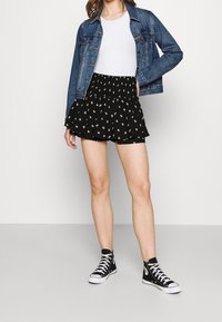 Gonna skater nera con stampa floreale bianca, orlo arricciato, abbinata a una maglia bianca e una giacca di jeans, completata da sneakers alte nere.